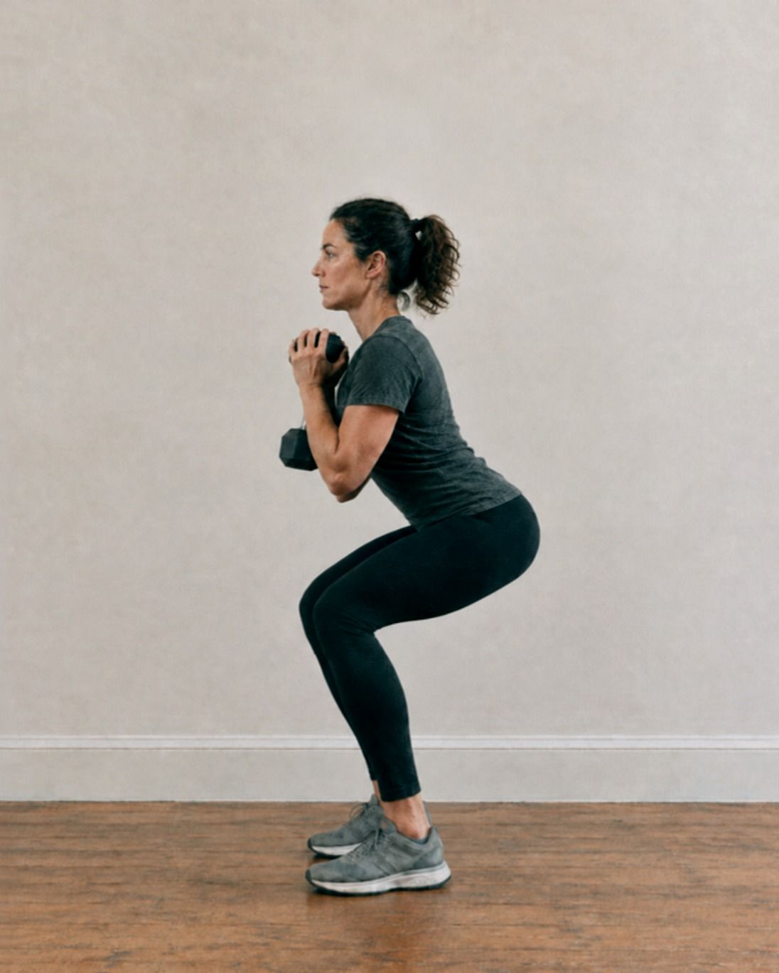 A woman lowers into a goblet squat holding a dumbbell at her chest.